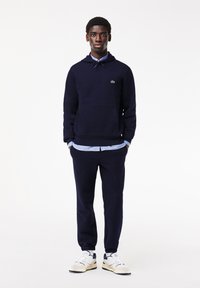 Felpa con cappuccio blu navy con tasca frontale, abbinata a pantaloni della tuta coordinati. Sneakers bianche con dettagli blu navy completano l'outfit.