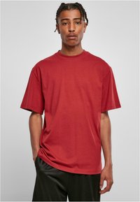 Tricou roșu din bumbac, cu mâneci scurte și guler tip crew, prezentând o croială lejeră și o textură fină. Fără modele sau grafice vizibile.