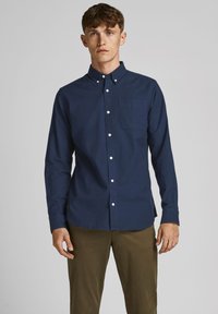 Camisa de manga larga de color azul marino, botón en algodón, con un bolsillo en el pecho, botones blancos y un cuello clásico, combinada con pantalones caqui.