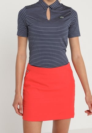 Marineblaue und weiße, gestreifte Kurzarmbluse mit Schlitz am Ausschnitt kombiniert mit einem knallroten Minirock mit seitlicher Reißverschlusstasche.