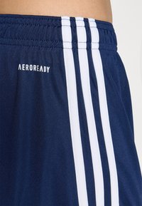 Mörkblå träningsshorts med en slät yta, med tre vita ränder längs sidorna och "AEROREADY"-logotypen i vitt.