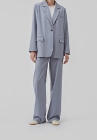 Costume bleu clair avec une veste taillée et un pantalon à jambes larges. Comprend une fermeture à un bouton et des poches latérales. Tissu lisse, design minimal.