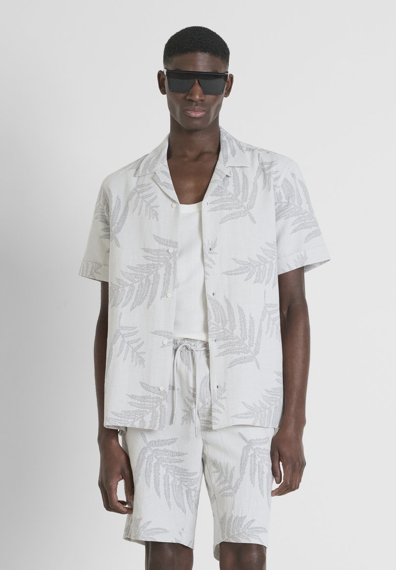 Conjunto de camiseta de manga corta y pantalones cortos en gris claro con un patrón de hojas, hecho de una tela texturizada. Combinado con gafas de sol negras.
