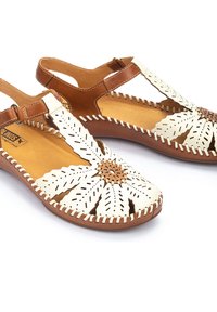 Sandales en cuir blanc avec un design floral découpé au laser, accents en cuir marron et coutures contrastantes. Ouvertes à l'avant avec une sangle ajustable.