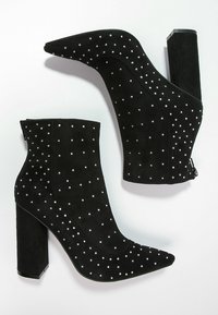 Schwarze Wildleder-Stiefeletten mit spitzer Kappe und Blockabsatz, verziert mit silbernen Nieten in einem verstreuten Muster. Reißverschlussdetail an einer Seite.