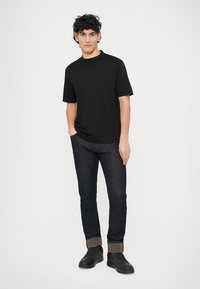 T-shirt preta de manga curta combinada com jeans azul escuro e ténis pretos, apresentando mangas dobradas e textura suave.