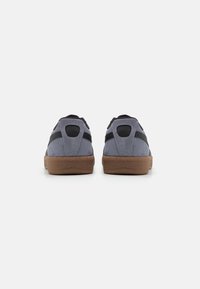 Gray suede sneakers with black accents, rear view. Features round heel tab and textured brown rubber sole. Simple design with no visible patterns.