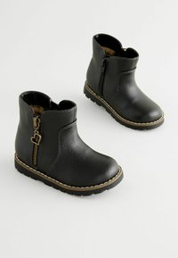 Schwarze Leder-Ankle-Boots mit seitlichem Reißverschluss, genähten Details und strukturiertem Obermaterial. Mit einer braunen Gummisohle für guten Halt.