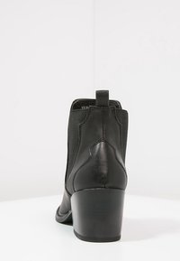 Stivale alla caviglia in pelle nera con pannelli laterali elasticizzati, dettagli a cucitura curvata e tacco impilato. Texture liscia con design classico.
