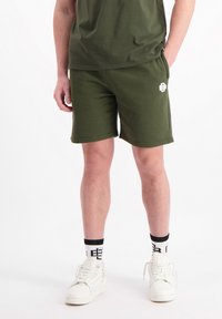 Groene katoenen shorts met een elastische tailleband en zijzakken. Witte logodetail op het linkerbeen. Gemaakt in combinatie met witte sneakers en gestreepte sokken.