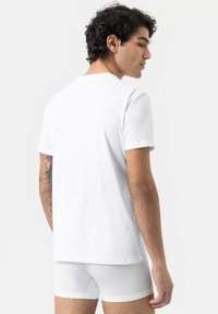 T-shirt en coton blanc à manches courtes et col rond, vu de dos. Le modèle a un tatouage sur le bras gauche.