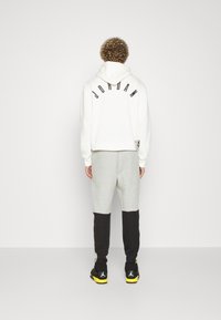 Vitt huva med "JORDAN" i svarta bokstäver på ryggen, tillsammans med grå och svarta sweatpants. Svarta sneakers med gula detaljer.