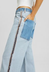 Ljusblå vida jeans med en sidosöm med kontrasterande sömnad och en bakficka. Tillverkade av denim med en blekt textur.