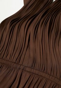 Tejido marrón con pliegues y una textura suave, que presenta una cinturilla fruncida para dar estructura. El color es profundo y uniforme en toda su extensión.