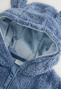 Blauwe fleece hoodie met een zachte buitenkant en een lichtblauwe voering met kleine pootafdrukken. Inclusief oorkappen op de capuchon.