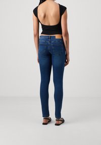 Jeans skinny blu con un lavaggio sbiadito, abbinati a una maglietta nera con un design a schiena scoperta. Cuciture notevoli su tasche e vita.