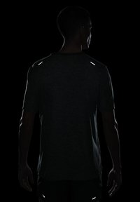 Camiseta atlética gris oscuro de mangas cortas, con acentos reflectantes en los hombros, textura suave y un ajuste relajado.