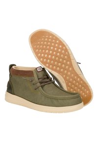 Botas de tela verdes con un cuello acolchado marrón, que presentan una suela de goma beige con un patrón de agarre texturizado y cordones marrones.