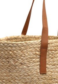 Sac en osier tissé avec des poignées en cuir marron. La couleur naturelle offre une texture avec des fibres visibles et des motifs de tressage.