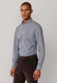 Camisa de botones a cuadros azul y blanca con cuello, con un logo sutil en el pecho. Combinada con pantalones de pana oscuros.