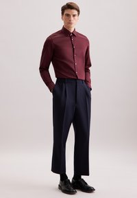 Camicia burgundy con colletto button-down, abbinata a pantaloni blu a pieghe e scarpe stringate nere, caratterizzata da una texture liscia.