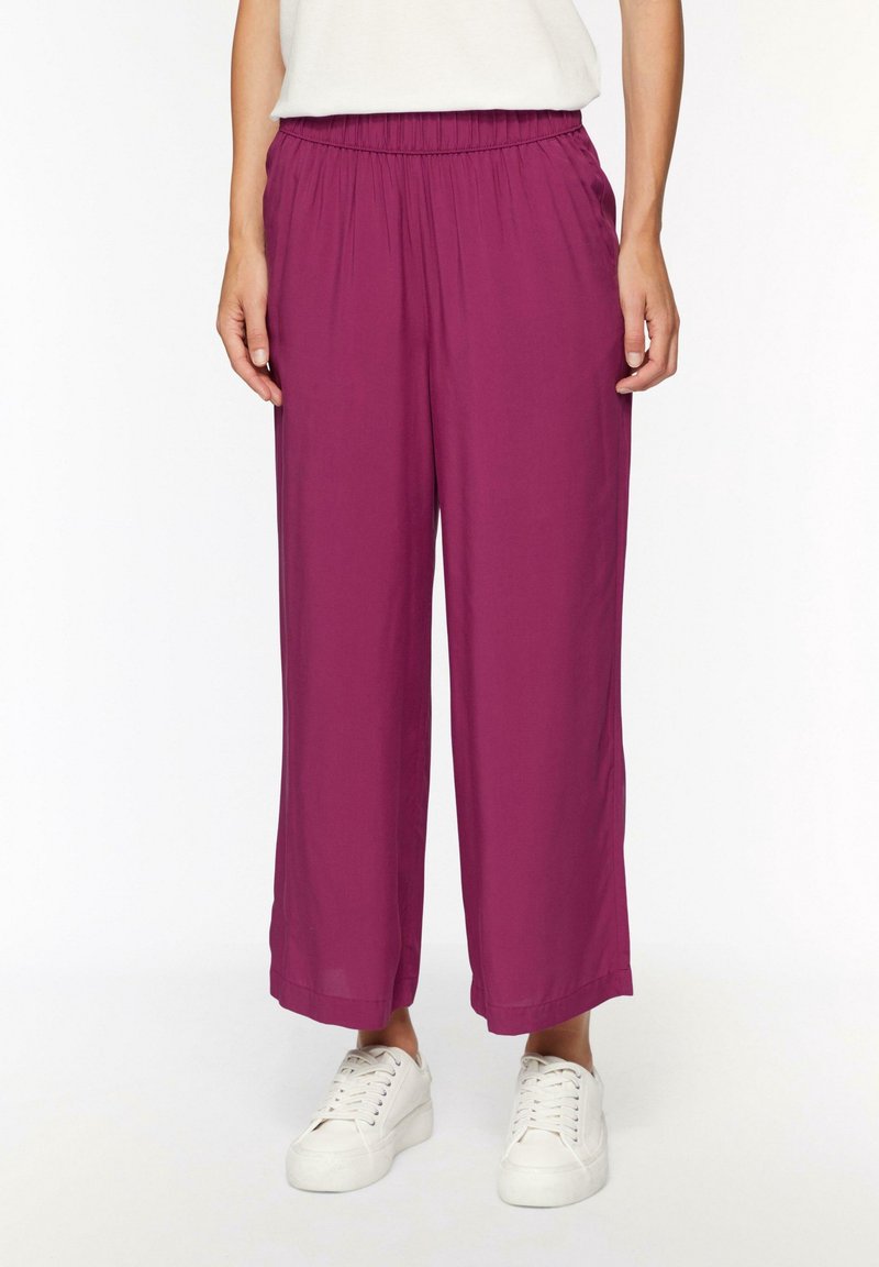 Pantalons larges fuchsia avec ceinture élastique, fabriqués en tissu léger. Portés avec des baskets blanches. Texture lisse, sans motifs visibles.