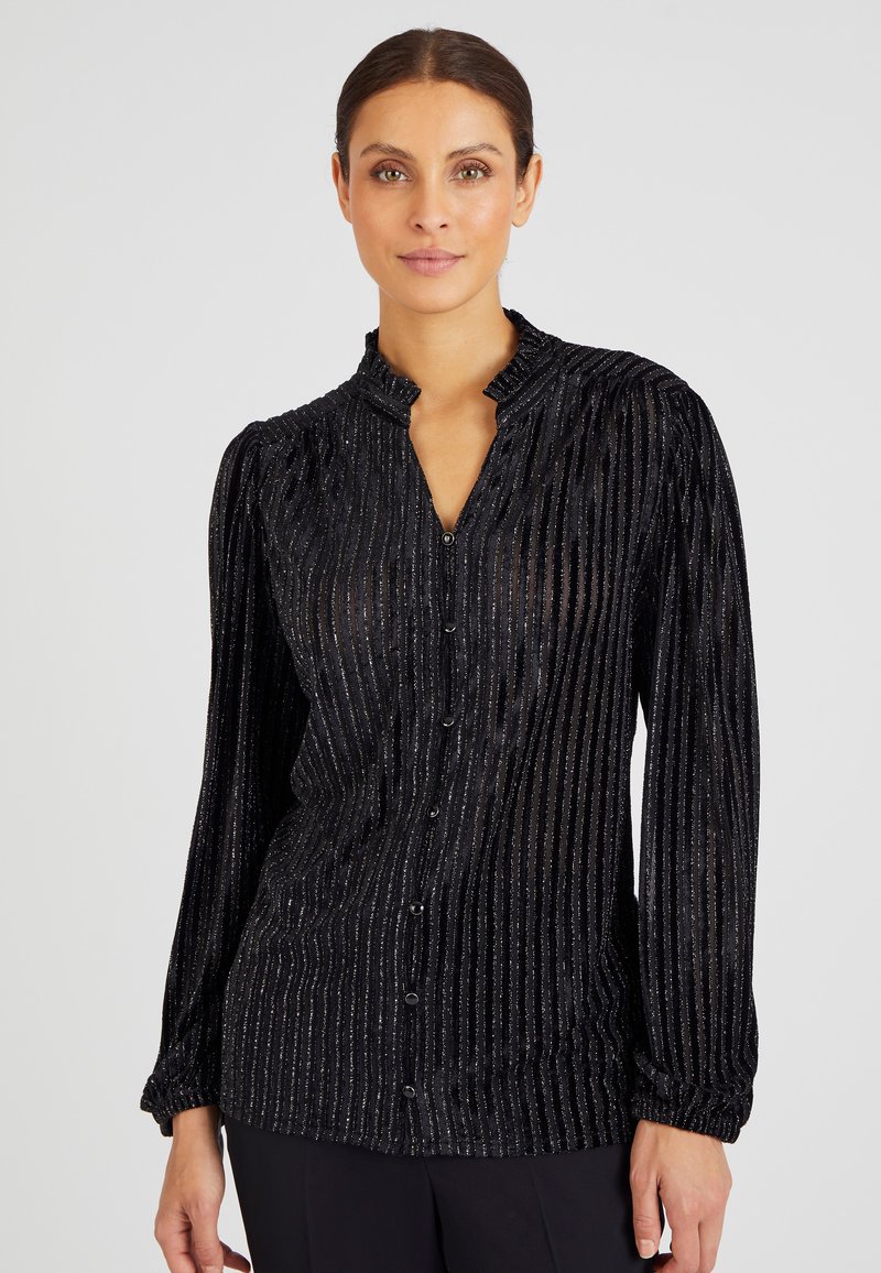 Blusa in velluto nero con colletto alto, maniche lunghe e strisce verticali argentate. Decorata con chiusura a bottoni sul davanti.