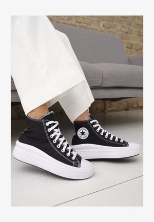 Sorte lerrets høy-top sneakers med hvite gummisulinger og snørebånd. Har et rundt logo på siden og kontrasterende hvite sting.
