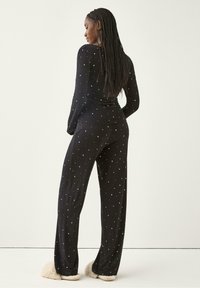 Sort pyjamasæt med lange ærmer og hvidt stjernemønster, der har en tætsiddende top og løse bukser. Blødt stof, båret med fuzzy slippers.