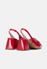Chaussures slingback en cuir verni rouge avec des talons en forme de cône. Dotées d'une surface texturée et d'un accent en noeud à l'avant.