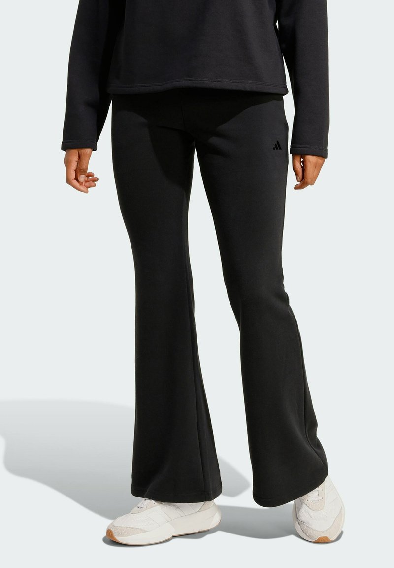 Černé rozšířené tepláky vyrobené z měkké, texturované látky se decentním logem Adidas na bocích. V kombinaci s bílými sportovními botami.