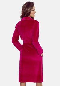 Accappatoio di velluto rosa con maniche lunghe, colletto, vita con cintura e tasche laterali. Texture morbida con un design di lunghezza al ginocchio.