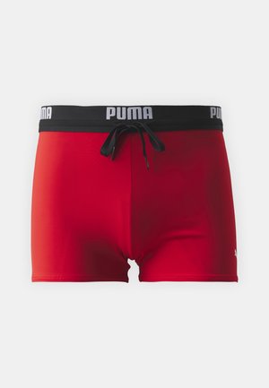 Shorts de bain rouges avec une taille noire ornée d'un texte logo blanc, cordon de serrage à l'avant et texture de tissu lisse.