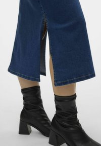 Denim krilo s ravnim krojem, temno modre barve, z detajli stranskega razporka, v kombinaciji z črnimi usnjenimi škornji do kolen s peto.