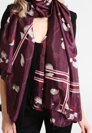 Écharpe violet foncé avec des motifs floraux blancs et rouges ainsi que des rayures, portée sur un haut noir et un blazer noir sur une personne.