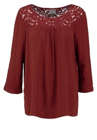 Blouse à manches longues rouge rouille avec détail en dentelle sur le plastron et col rond, coupe ample avec de légers fronces sous le panneau en dentelle.