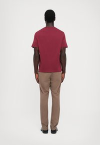 Maronfarvet kortærmet t-shirt med rund hals. Bæres med lysebrune bukser og sorte sko, vist fra ryggen mod en hvid baggrund.