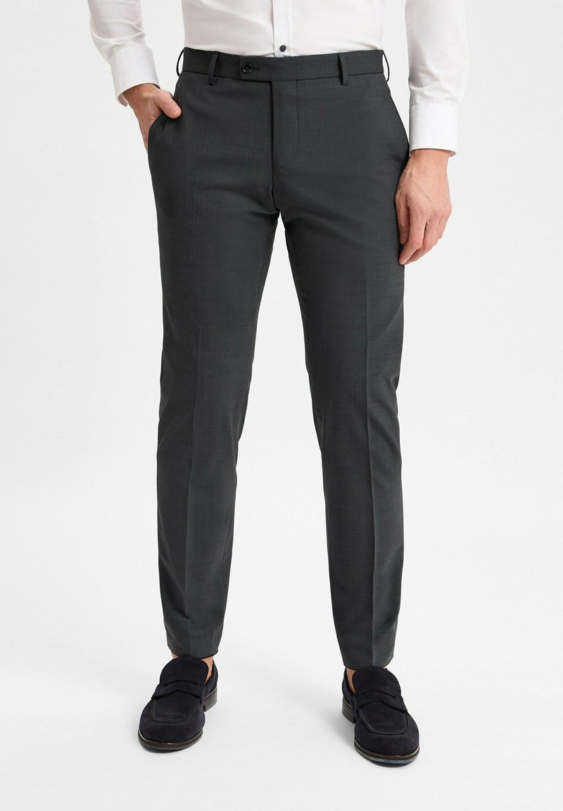 Graue, maßgeschneiderte Hosen mit glatter Textur, flacher Vorderseite und seitlichen Taschen, kombiniert mit dunkelblauen Slippern.