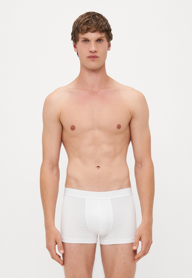 Boxer-briefs en coton blanc portés par un modèle, offrant une coupe ajustée et une ceinture douce. Le tissu est lisse avec des détails de couture minimes.