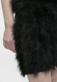 Μαύρο φόρεμα με υφή, που διαθέτει μακριά, απαλή επένδυση από συνθετική γούνα κατά μήκος των πλευρών, σε αντίθεση με τη λεία βάση από ύφασμα.