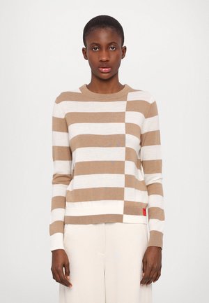 Stripet genser med beige og hvite horisontale striper, rund hals, lange ermer, myk tekstur og et rødt merke i nederkanten.