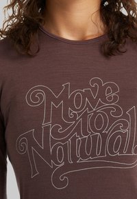 Ruskea pitkähihaisessa paidassa on valkoinen teksti, jossa lukee "Siirry luonnolliseen". Paidassa on pehmeä pinta ja istuva kaula-aukko.