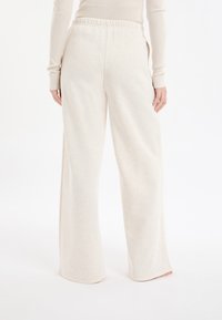 Spodnie dresowe o szerokich nogawkach w jasnobeżowym kolorze, z elastycznym pasem i bocznymi kieszeniami, wykonane z miękkiego, teksturowanego materiału z delikatnym melanżowym wzorem.