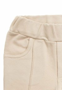 Beżowe spodnie dresowe o miękkiej fakturze, z elastycznym pasem, boczną kieszenią i przeszyciami wzdłuż szwów.