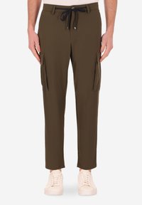 Pantaloni cargo verde oliva con vita regolabile, vestibilità slim, due tasche laterali e tessuto testurizzato. Le scarpe sono sneakers bianche.