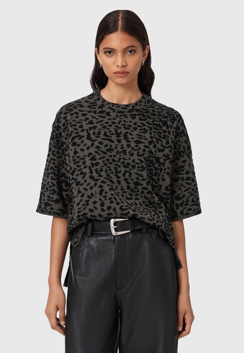 Vrouw in een grijs en zwart luipaardprint t-shirt met korte mouwen, ingestopt in een zwarte leren broek met hoge taille en een zwarte riem.