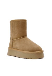 Bottine en daim brun clair avec semelle plateforme épaisse et bout arrondi, présentant des coutures apparentes et une semelle extérieure crantée.