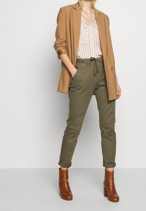 Brun blazer, randig ljus skjorta, olivgröna smala byxor och bruna ankelläderskor. Har en avslappnad passform och uppvikta ärmslut.