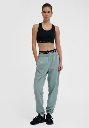 Sort sports BH med scoop halsudskæring og logo bånd; lys mintgrønne joggers med elastisk talje og manchetter; sorte sneakers.