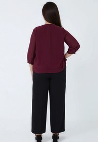 Bordeauxblouse met driekwartmouwen, gemaakt van lichte stof, gecombineerd met losse zwarte broek, met een rechte snit en een relaxte pasvorm.